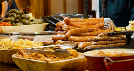 Street food vendor presenting steaming sausages and golden fried potatoes at festive Christmas market, offering traditional local winter cuisine