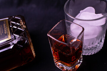 Top side view of liquor in a cup and brown liquor in a bottle. The frame also has a cup of ice in a cocktail glass. 