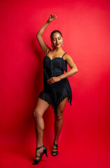Woman in a black fringed dress dancing salsa on a vibrant red background