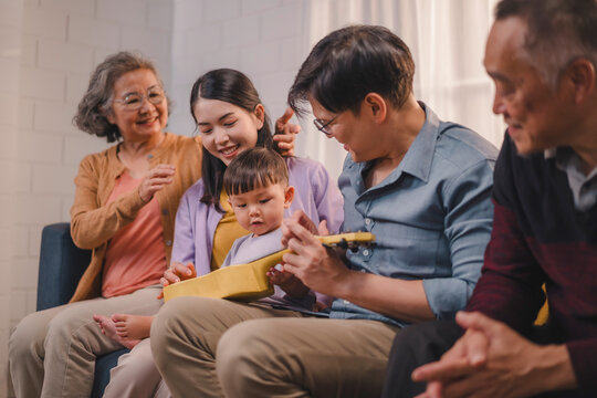 Happy multigenerational family enjoying quality time together at home, smiling and bonding while teaching a toddler to play ukulele, showing love, parenting, and cultural values across generations. - Powered by Adobe