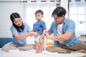 Asian parents helping their toddler get dressed after bath in a cozy bedroom. A warm family moment showing love, baby care routine, and teamwork in modern parenting.