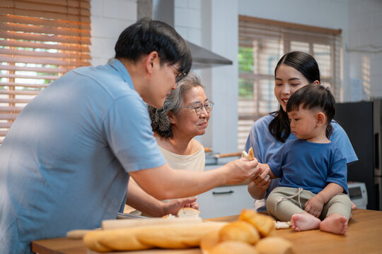 Asian father playfully entertains his toddler with a slice of bread in a cheerful kitchen setting. Fun family interaction capturing love, laughter, and warm bonding in modern parenting.