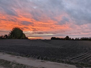 A scenic view of a field and a colorful sky at sunset. The sky displays vibrant hues of orange and red, suggesting the end of the day, with soft clouds floating above the field.