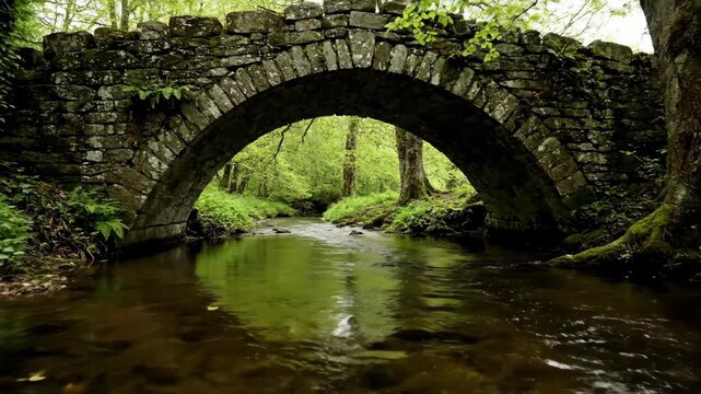 Old stone bridge crossing a gentle stream in lush green landscape