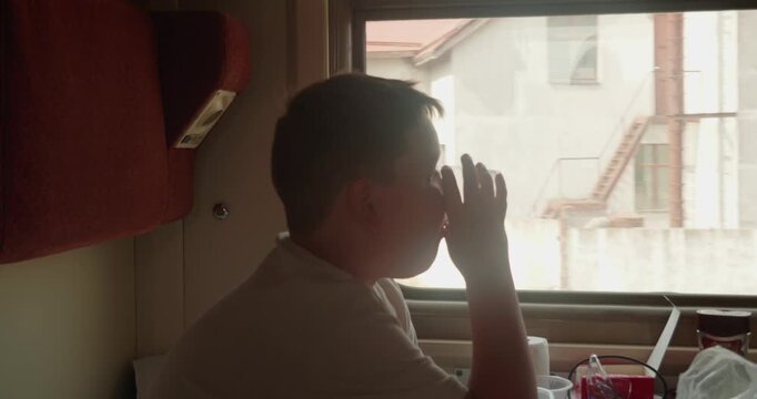 A pensive boy sits in a sleeper train compartment drinking from a glass and watching the scenery pass by the window during a long train ride enjoying the quiet ride The child is traveling on a train.