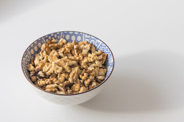 Shelled Walnut Kernels in a Blue and White Patterned Bowl on a White Background