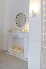 White Christmas interior with decorated tree, glowing garlands, candles, white gifts, elegant festive decor, and a round mirror above a white fireplace.