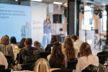 Fototapeta premium Audience attends blurred conference talk with speaker on stage in bright venue.
