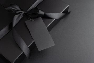 Black Gift Box with Satin Ribbon and Blank Tag on Dark Background