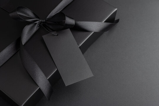 Black Gift Box with Satin Ribbon and Blank Tag on Dark Background