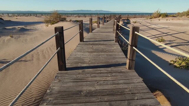 Strolling at sunset along a wooden boardwalk over the beach dunes. Time Lapse. Wooden walkways installed to protect the dunes and their flora and fauna, on Riumar beach in Catalonia, Spain