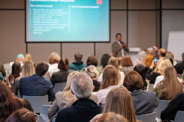 Obraz premium Engaged audience at business conference listening to speaker in modern lecture hall with projector screen