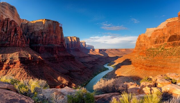 a dramatic canyon with towering red rock cliffs a winding river carving through the rugged terrain golden sunlight highlighting the deep textures vast open sky above