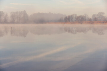 Fototapeta premium Misty Morning on the Lake with Distant Trees, Poland, Background or Wallpaper