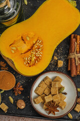 Half butternut squash on a dark tray with baking ingredients. Sugar, cinnamon sticks, ginger, nutmeg