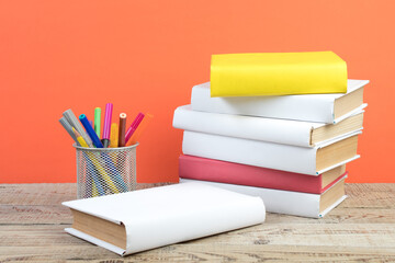 Books stacking. Books on wooden table and orange background. Back to school. Copy space for ad text.