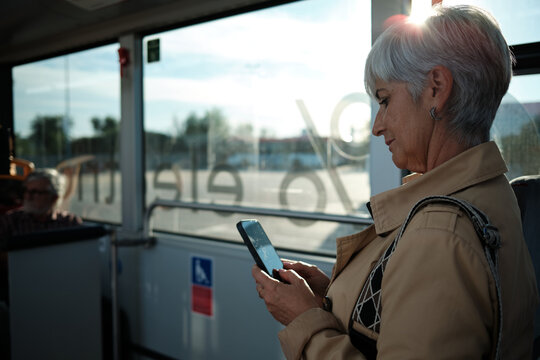 Senior woman using smartphone while traveling on public bus
