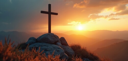 Wooden cross on rocky mountain peak at sunrise. Golden sun rays shine through clouds illuminating vast mountain ranges. Spiritual symbol against dawn sky.