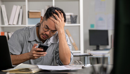Businessman looking stressed while using phone, Businessman working at office feels overworked and...