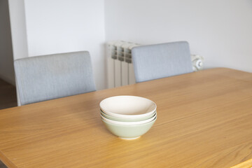 Stack of pastel bowls on wooden table. Simplicity, calmness, and domestic comfort in everyday modern interior.