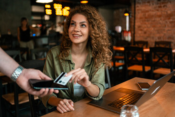 Young woman making a payment while sitting at a modern cafe with a laptop