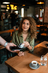 Young woman enjoying coffee while making a payment at a cafe during afternoon hours