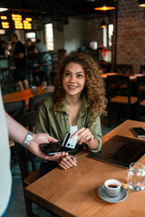 Young woman enjoying coffee while making a payment at a cafe during afternoon hours