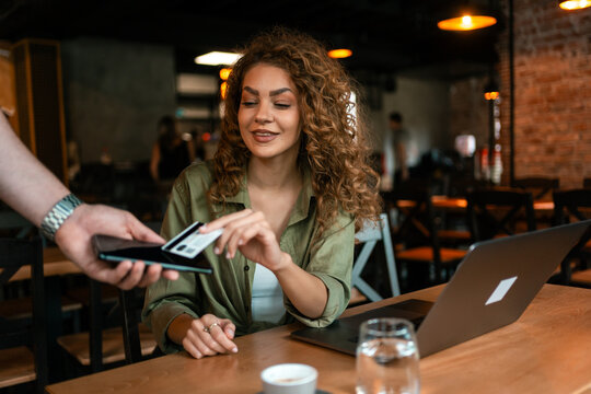Woman using laptop in cafe while receiving payment on smartphone during late afternoon