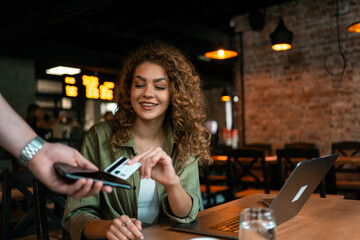 Young woman enjoying a coffee while paying for her order in a modern cafe
