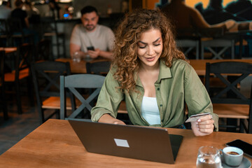 Young woman working on a laptop in a lively cafe while holding a credit card