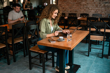 Young woman works on laptop while enjoying coffee in a cozy cafe setting during daytime