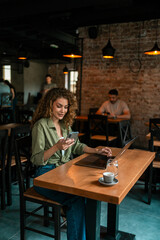 Woman working on laptop while using smartphone in a cozy cafe setting