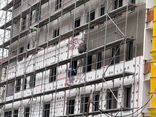 Workers applying insulation on building facade. Progress, human labor, and collaboration in architectural renewal and construction process.