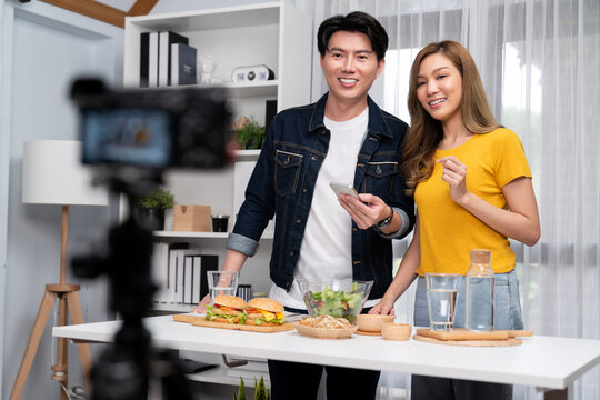 Chef influencers reading comment on phone for answer time on social media cooking show channel live streaming menu dish mix salad, bun bread wholegrain and hamburger record by video camera. Infobahn.
