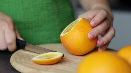 Close up of female hand cutting a fresh orange fruit on wooden cutting board - Powered by Adobe