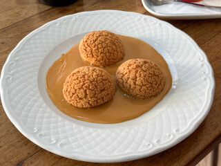 Cream puff dessert served with caramel sauce on a white plate. Sweet indulgence, comfort, and harmony of taste and texture in a cozy cafe moment.