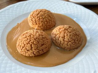 Close-up of three caramel cream puffs on plate with glossy sauce. Dessert elegance, texture, and sweetness reflecting cozy atmosphere of afternoon treat.