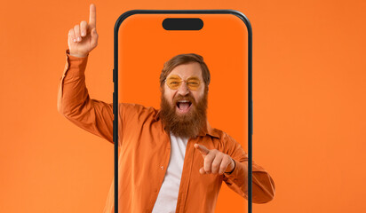 A man with a beard and glasses joyfully points and raises his finger, standing behind a large...