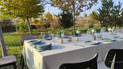 Elegant outdoor dining setup with plates and glasses in sunlit garden.