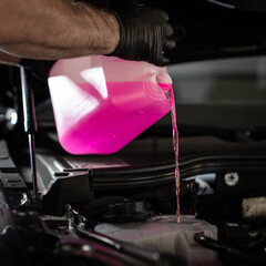 Man pouring liquid from plastic canister into car washer fluid reservoir, closeup