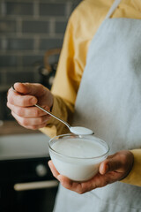Close-up of man wearing a yellow shirt and an apron holding yogurt in a bowl