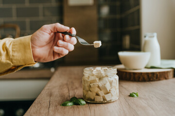 Man eating tofu cubes from jar on a wooden table