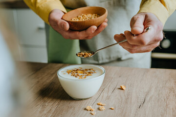 Close up of man adding granola to yogurt bowl