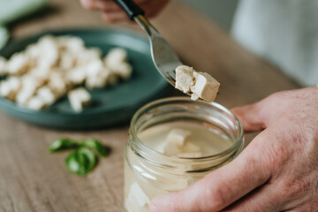 Males hands holding tofu on a fork over a jar