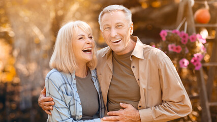 A happy couple stands together in a vibrant garden filled with flowers as they share a moment of laughter in the warm autumn sunlight. Their smiles radiate joy.
