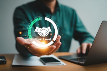 Man presenting trust level graphic with handshake icon while using a laptop on a wooden desk