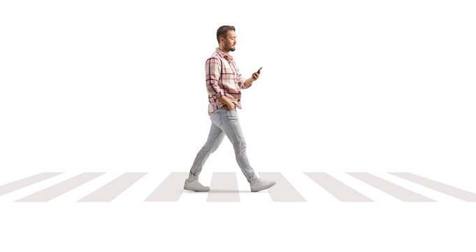 Full length profile shot of a man in checkered shirt holding a smartphone and crossing at zebra