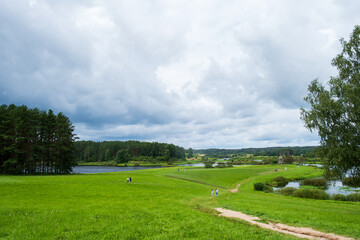 Obraz premium Scenic Meadow with People Strolling Under Cloudy Sky