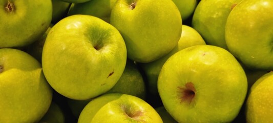 Vibrant close-up photograph of a pile of fresh green apples, showing their smooth texture and natural shine