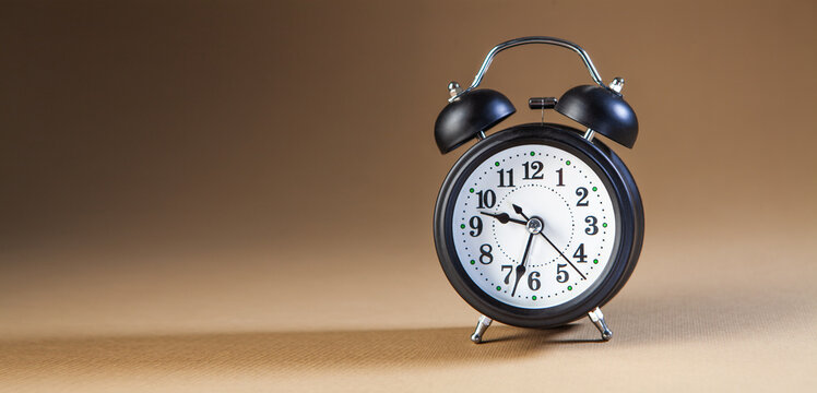 Classic black alarm clock on brown background. Time is money concept.
